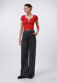 Haut court côtelé rouge à manches courtes, avec un col blanc et un lien ajustable à l'avant. Associé à un jean noir taille haute à jambe large.