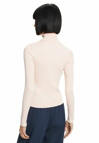 Suéter de cuello alto de canalé en rosa claro con mangas largas, diseño ajustado y textura suave, combinado con pantalones de pierna ancha en color marino.