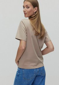 Beige t-paita lyhyillä hihoilla pehmeästä kankaasta, pyöreä pääntie, yhdistettynä sinisiin korkeavyötäröisiin farkkuihin. Sileä rakenne, yksinkertainen muotoilu.