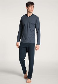 Navy gestreepte long-sleeve top met een borstzak, gecombineerd met effen navy broek. Zachte stof met een ontspannen pasvorm, geen zichtbare sluitingen.