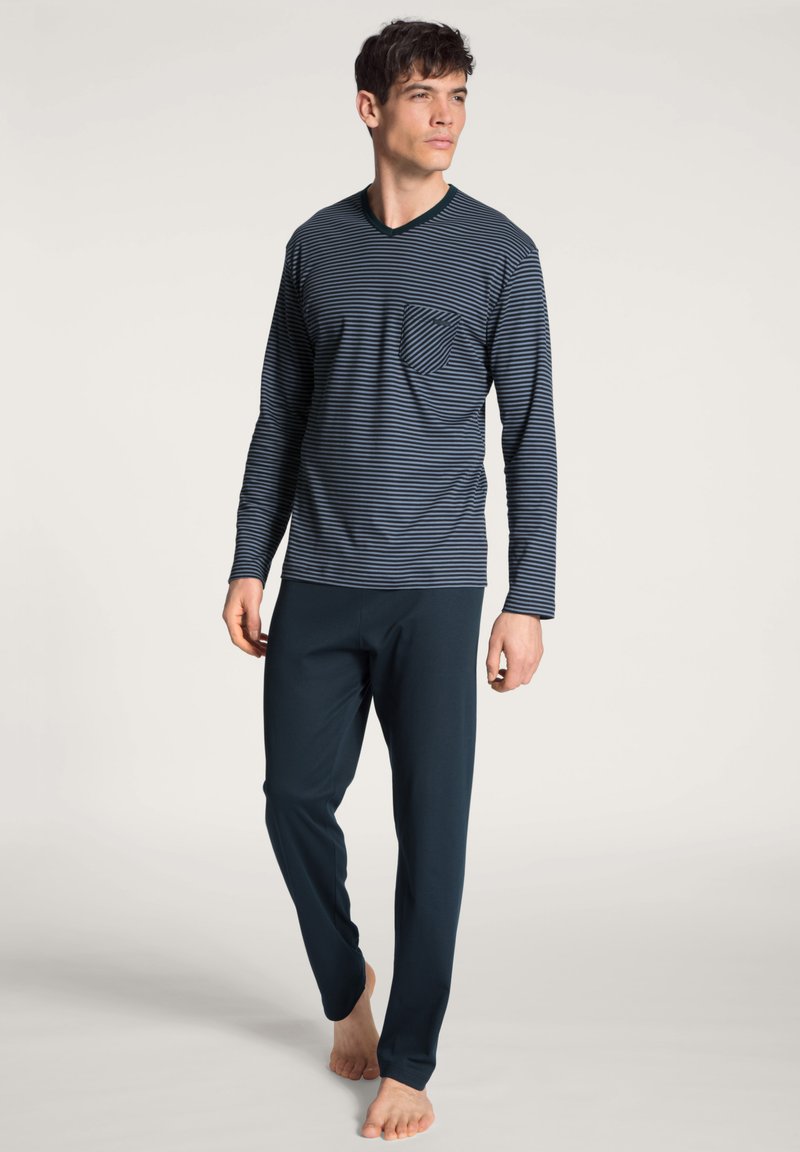 Navy gestreepte long-sleeve top met een borstzak, gecombineerd met effen navy broek. Zachte stof met een ontspannen pasvorm, geen zichtbare sluitingen.