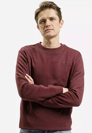 Bordowy sweatshirt z okrągłym dekoltem i ściągaczami. Posiada małe logo na klatce piersiowej. Miękka tkanina o gładkiej fakturze.
