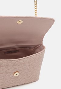 Bolso de mano acolchado rosa con una correa de cadena, que presenta un cierre de botón a presión dorado y un forro interior suave. Dentro hay un bolsillo etiquetado "ANNA FIELD."