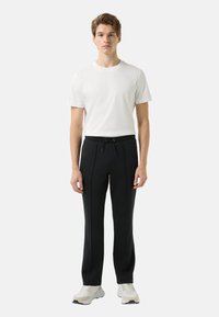 Czarne spodnie sportowe z elastycznym pasem i sznurkiem do wiązania, z dwoma pionowymi szwami. Połączone z dopasowaną białą koszulką i jasnymi trampkami.
