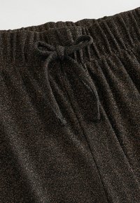 Mustad püksid elastse vöökohtaga, millel on seotud pael. Kangas on tekstuuriga viimistlusega ja sellel on kuldse metallilise sädelusega kirjutisi.