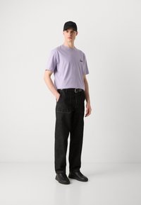 Lyse lilla bomulds-T-shirt med lille logo, parret med sorte denimbukser med forlommer og sorte sneakers. En sort kasket tilføjer detalje.