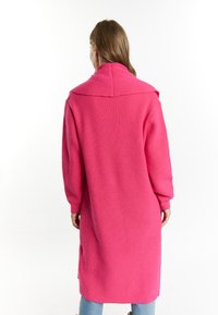 Rosa stickad lång kappa med bred krage, lösa ärmar och en texturerad tyg. Har sidofickor och rak passform.