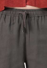 Pantalones de un gris oscuro, texturizados, con una cinturilla elástica y cordón. La tela presenta un sutil patrón de tejido. Sin bolsillos visibles.