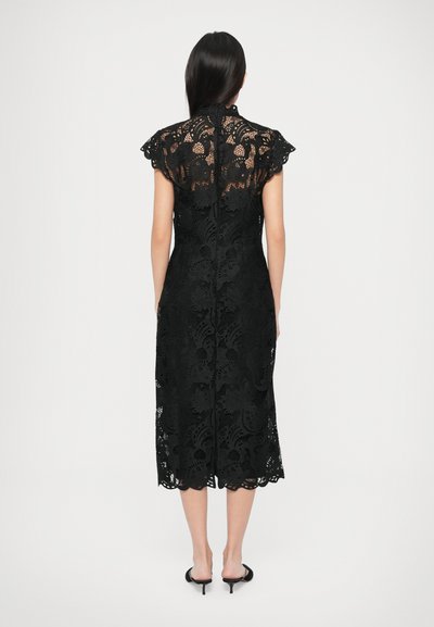 Czarna koronkowa sukienka z krótkimi, falbaniastymi rękawami, ozdobiona kwiatowym wzorem i falistym dołem. Sukienka sięga do połowy łydki i ma wysoki dekolt.