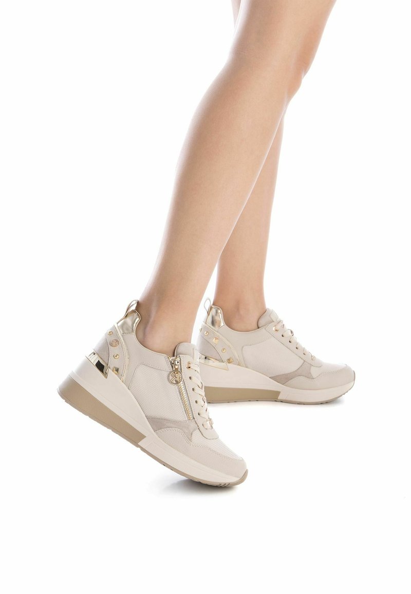 Zapatillas estilo cuña beige que combinan materiales de malla y piel sintética, con detalles dorados, cordones, cremallera lateral y suela texturizada.