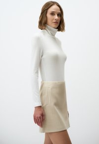 Enganliegender weißer Rippstrick-Turtleneck kombiniert mit einem beigen, strukturierten Minirock mit einer Seitentasche.
