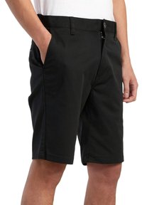 Pantalones cortos negros de tela de algodón mezclado, con cierre de cremallera, pasadores para cinturón y bolsillos laterales. Textura suave con un diseño ajustado.