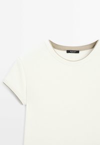 T-shirt beige clair à manches courtes avec un col rond et un bord de col beige contrastant. Fabriqué en coton doux.