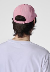 Rosa bomull baseballkeps med en böjd skärm, justerbart band bak, och synliga sömnadsdetaljer, bärs med en vit t-shirt.