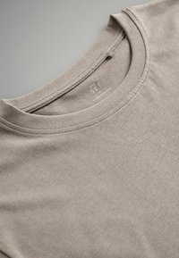 Bawełniany t-shirt w kolorze taupe z okrągłym dekoltem. Charakteryzuje się miękką fakturą i minimalistycznym wzornictwem. Metka umieszczona na tylnej części kołnierza.