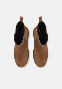 Paire de bottines en daim marron avec fermetures éclair latérales, languettes à l'arrière et doublure intérieure noire, vue de dessus sur un fond blanc.