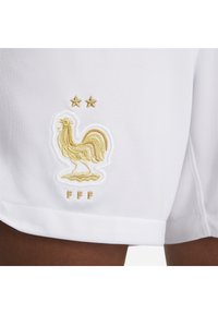 Shorts blancs ornés d'un logo de coq doré brodé, de deux étoiles dorées au-dessus et de "FFF" en or sous le coq.