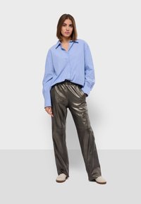 Blauw gestreept overhemd met een losse pasvorm, gecombineerd met glanzende grijze metalen brede broek en crème kleurige sneakers.