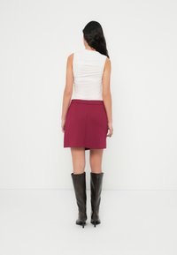 Λευκό αμάνικο τοπ με υφή στην πλάτη, συνδυασμένο με μίνι φούστα σε μαρόν χρώμα και μαύρες δερμάτινες μπότες μέχρι το γόνατο. Απλός και μοντέρνος σχεδιασμός.