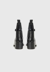 Bottes de cheville en cuir verni noir avec une sangle et un détail de boucle, dotées d'un dessus texturé et d'un talon bloc modéré.