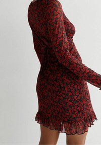 Schwarzes Langarmkleid mit rotem Blumenmuster, das einen gerafften Saum und transparente Stoffe für eine zarte Textur aufweist.