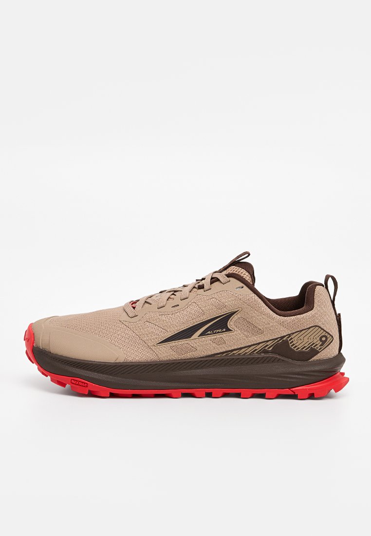 Zapatilla de trail running beige con una parte superior de tela texturizada, acentos en marrón oscuro y una suela exterior roja brillante que presenta tacos prominentes para agarre.