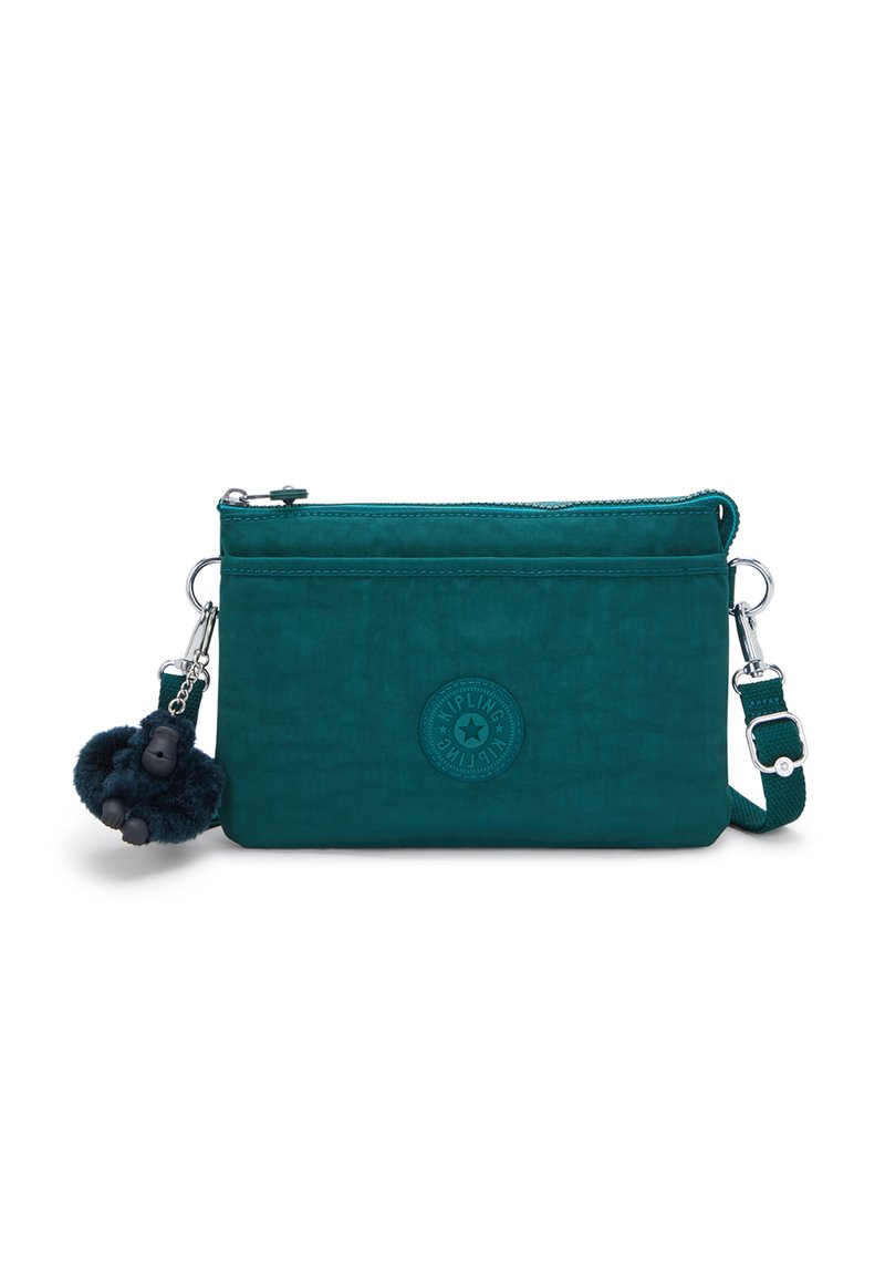 Teal skuldertaske lavet af struktureret stof, med lynlåslukning, justerbar rem og en fluffy pom-pom charm. Rundet logo accent synlig.