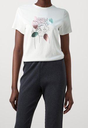 Personne portant un t-shirt blanc avec un dessin minimaliste au trait représentant un visage de femme, des fleurs et des formes abstraites colorées sur le devant.