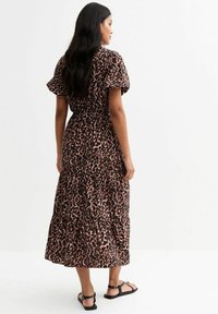 Maxi-jurk in roze en zwart luipaardmotief, met korte gerimpelde mouwen, een elastische taille en een gelaagde rokontwerp. Platte sandalen gedragen.