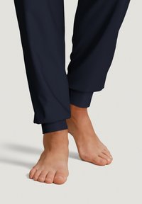 Navy sweatpants with a smooth texture, gathered cuffs, and bare feet positioned near the hem. Focus on fabric and design elements.