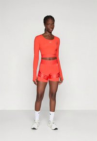 Czerwony długi crop top z długim rękawem i dopasowane szorty z elastycznego materiału, z nadrukiem "NIKE PRO" i dopasowanym krojem. Białe trampki i skarpetki.