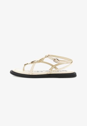 Sandalo piatto beige con suola nera, punta aperta, sottili cinturini, decorazioni ovali dorate e fibbia regolabile alla caviglia.