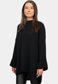 Maglione nero oversize a maglia con una trama a coste, collo alto e maniche a campana. L'orlo è asimmetrico, più lungo sul retro.