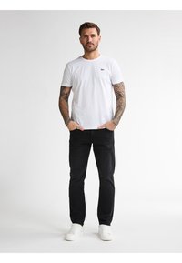 Witte katoenen t-shirt met een ronde hals en een klein geborduurd logo, gecombineerd met zwarte spijkerbroek en witte sneakers.