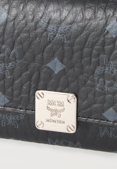 Cuir noir texturé avec des logos MCM bleu clair et une plaque carrée en argent gravée de "MCM" et "München" sur un coin du sac.