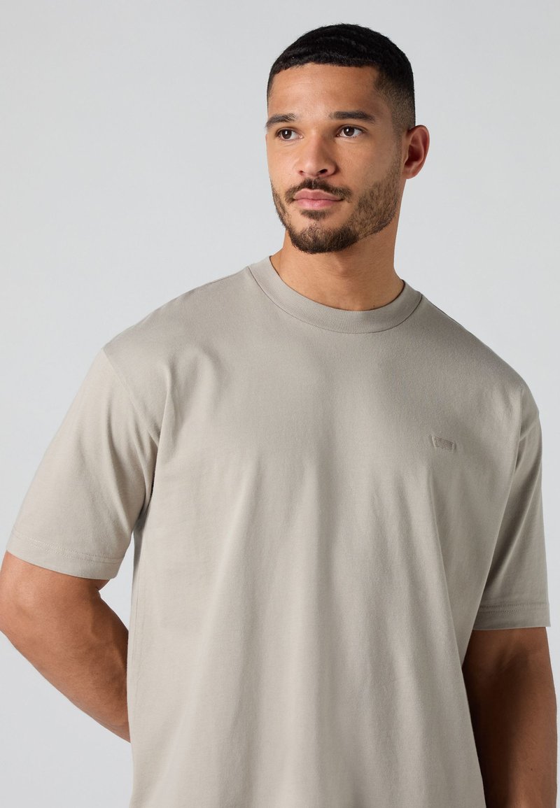 Kurzärmliges, hellbeiges T-Shirt aus Baumwolle. Mit Rundhalsausschnitt, weichem Material und kleinem Logo auf der Brust.