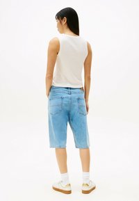 Lichtblauwe denim shorts met een relaxte pasvorm, voorzien van achterzakken en een licht vervaagde textuur; gecombineerd met een witte mouwloze top en witte sokken.