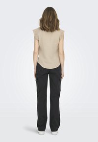 Haut beige texturé avec des manches festonnées, associé à un pantalon cargo noir avec poches latérales et coupe décontractée. Des baskets blanches complètent la tenue.