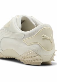 Weißer Sportschuh mit einem Mesh-Obermaterial, glatten Kunststoffakzenten und einer strukturierten Gummisohle mit kleinen Erhebungen für zusätzlichen Halt.