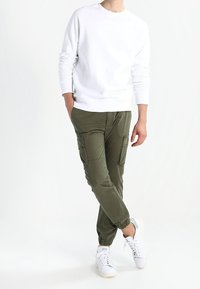 Felpa bianca a girocollo, pantaloni verdi oliva con tasche cargo e sneakers bianche con dettagli azzurri. Look casual e vestibilità rilassata.