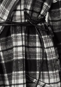 Bata de cuadros en blanco y negro de tejido suave, con un cinturón de material negro elegante, cuello estructurado y trama texturada.