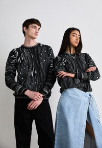 Zwarte gebreide truien met witte patronen, gecombineerd met zwarte jeans en een lichtblauwe denim rok met een zijslit en strikdetail.