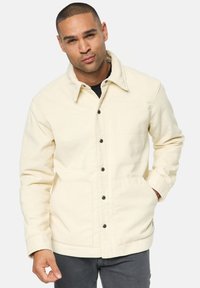 Helles beige Cordjackett mit Kragen, vorderem Knopfverschluss und zwei Seitentaschen. Weiche Textur mit strukturiertem Design.