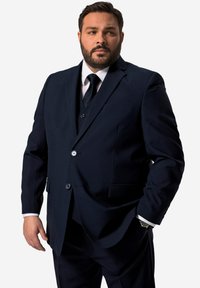 Abito blu navy con una vestibilità a un bottone, due bottoni e rever a punta. Indossato sopra una camicia bianca e una cravatta nera, con una leggera lucentezza.