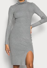 Robe en tricot côtelé gris avec col roulé, manches longues et fente haute sur la cuisse, présentant une silhouette ajustée et une texture en tricot douce.