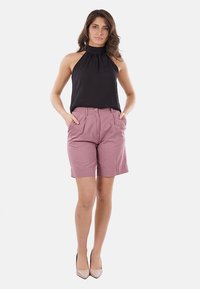 Top a fascia nero e pantaloni corti plissettati rosa chiaro con tasche, abbinati a tacchi beige. Tessuto morbido, vestibilità casual e dettagli hardware minimi.