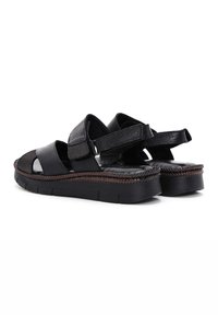 Black leather sandals featuring adjustable straps, open toe, and a thick, textured sole with braided accent detailing.