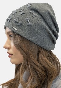 Cappello di lana grigio con applicazioni floreali e accenti di perle, caratterizzato da un design morbido e una texture liscia. Etichetta di branding sottile visibile.