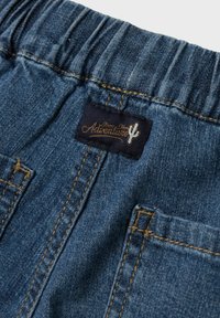 Shorts en denim avec une taille élastique, présentant une teinte bleu foncé, des coutures visibles et une étiquette avec le mot "Aventure" accompagnée d'un design de cactus.