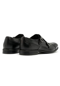 Zapatos de cuero negro con un acabado suave y cierre de hebilla simple. Presentan una puntera redondeada y sutiles detalles de costura en el talón.